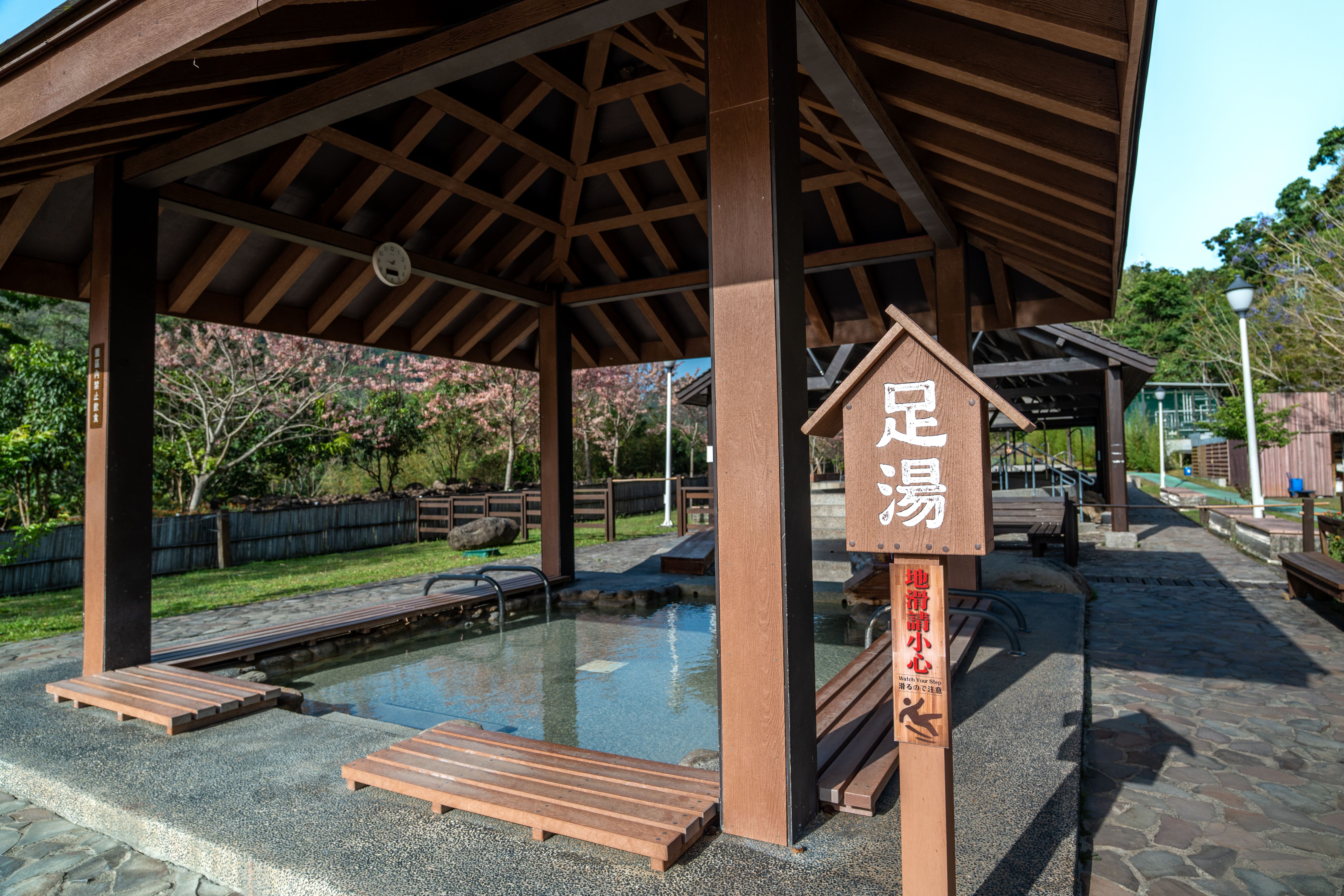 知本溫泉區的公共足湯,木亭下立著「地滑請小心」的告示——雨天泡湯,腳步放慢一點(實景)